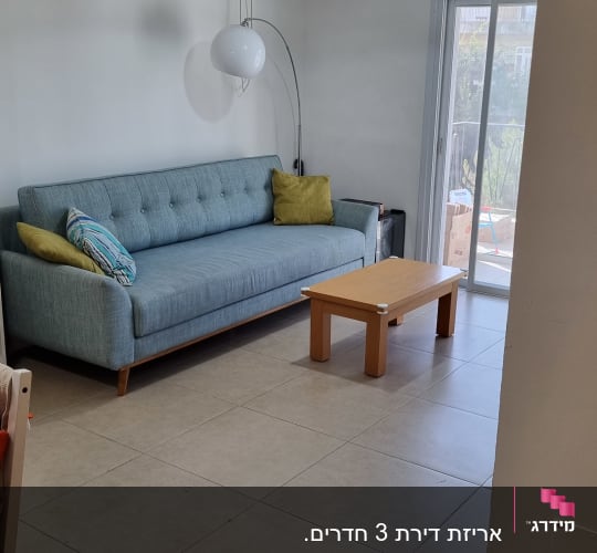 ספה כחולה עם כריות, שולחן עץ קטן, מנורה תלויה